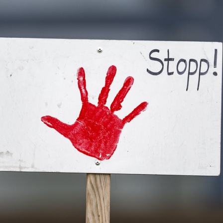 Auf einem weißen Schild ist ein roter Handabdruck sowie der Schriftzug "Stopp!".