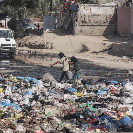 Zwei Mädchen tragen in Dair El balah Wasserkanister über eine mit Mülltüten verunreinigte Straße. 