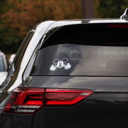 Ein Mickey-Mouse-Aufkleber mit Mittelfinger-Geste ist auf der Heckscheibe eines VW Golf zu sehen.