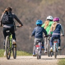 Eine Frau ist mit drei Kindern auf dem Fahrrad unterwegs auf einem Feldweg.