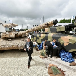 Männer in Anzügen und Reinigungspersonal vor Panzern auf der Rüstungsmesse Eurosatory in Paris.
