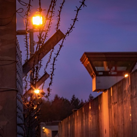 Außenansicht einer gefängnismauer bei Nacht mit Stacheldraht und Wachturm