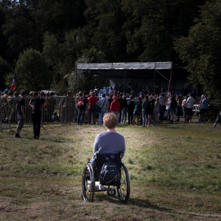 Frau im Rollstuhl am Rande einer Menschenmenge