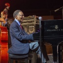 Der amerikanische Pianist Ramsey Lewis spielt lächelnd einen Flügel auf der Bühne.