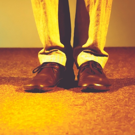Schuhe einer Person, die alleine auf der Bühne im Scheinwerferlicht steht.