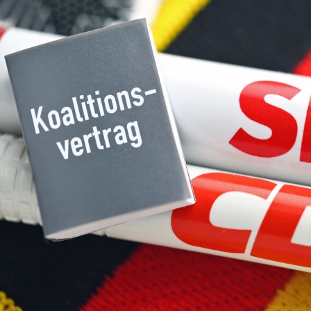 Zwei Stifte mit der Aufschrift SPD und CDU, dazu ein kleines graues Büchlein mit dem Schriftzug Koalitionsvertrag.