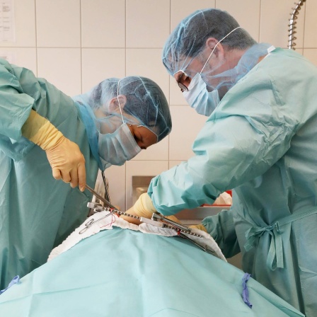 Zwei Mediziner stehen über einem Menschen und operieren im Brustbereich am Herzen.