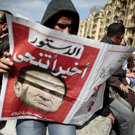 Husni Mubarak ist zurückgetreten; ein Mann liest die Meldung in der Zeitung. Menschen feiern am 12. Februar auf dem Tahrir-Platz in Kairo / Ägypten
