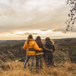 Drei junge Frauen sind mit dem Rücken zur Kamera zu sehen und stehen in der Landschaft. 