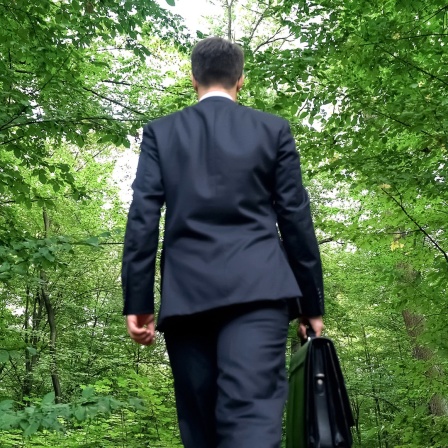 Der Blicke auf einen Geschäftsmann von hinten, der durch den Wald geht.