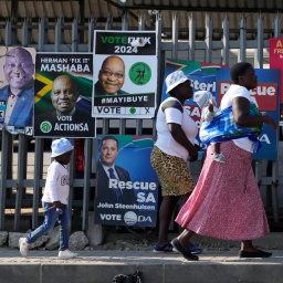 Das Beitragsbild des Dok5 Feature "Mandelas Erben - Südafrikas junge Generation ringt um die Zukunft" zeigt Frauen mit Kindern die an Wahlplakaten in Johannesburg vorbeigehen.