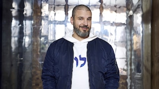 Rapper Ben Salomo steht vor einer Glasbausteinwand