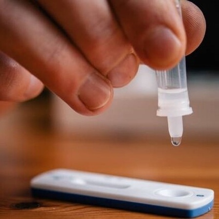 Eine Person träufelt die Probelösung eines Corona-Schnelltests auf die Testkassette