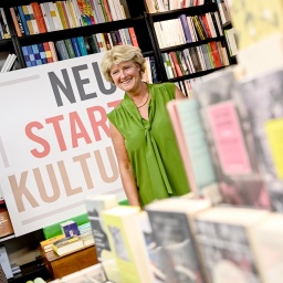 Kulturstaatsministerin Monika Grütters steht inmitten vieler Bücher in einer Buchhandlung, neben ihr ein Schild mit der Aufschrift "Neustart Kultur".