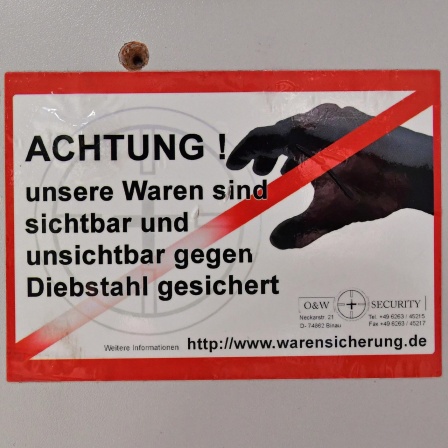 Ein Aufkleber mit der Aufschrift "Achtung ! unsere Waren sind sichtbar und unsichtbar gegen Diebstahl gesichert" ist an der Umkleidekabine in einem Sportgeschäft zu sehen