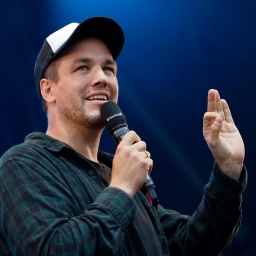 Comedian und Synchronsprecher Jan van Weyde, auf einer Bühne mit Mikrofon in der Hand.