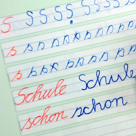 Hand schreibt das Wort Schule in Schreibschrift in ein Grundschulheft.
