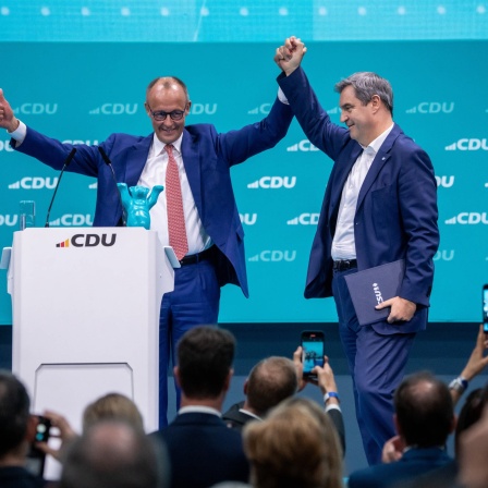 CDU-Chef Merz hält beide Arme auf einer Parteiveranstaltung nach oben - mit einer Hand hält er die von CSU-Chef Söder.