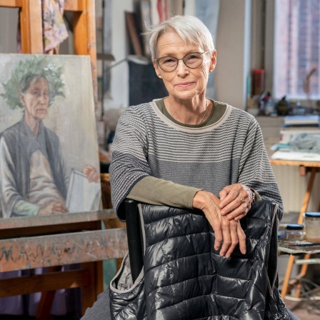 Die Leipziger Malerin Doris Ziegler in ihrem Atelier im Stadteil Plagwitz. Sie schaut in die Kamera. Im Hintergrund ist ihre Malerei zu sehen.