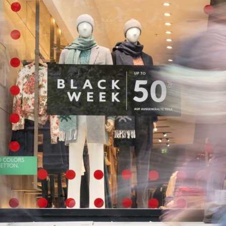 Werbung für den "Black Week Sale" hängt in einem Schaufenster, an dem Passanten vorbeigehen