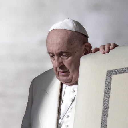 Papst Franziskus hält sich an einem Stuhl fest.
