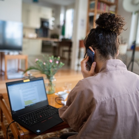Eine Frau nimmt von ihrem Wohnzimmer aus an einer Telefonkonferenz teil.