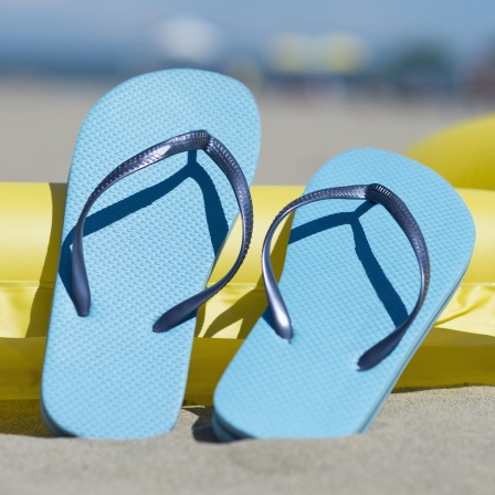 Blaue Flip-Flops und eine gelbe Luftmatratze am Strand. Symbolbild