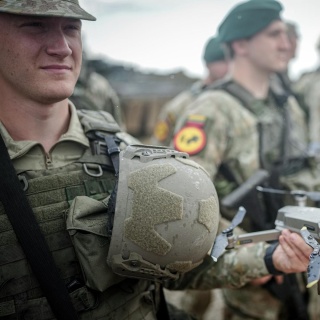 Ein Soldat hält eine Drohne in der Hand. Im Hintergrund sind weitere Soldaten zu sehen.