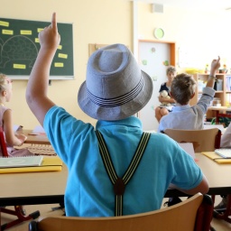 Junge mit Hut und Hosenträgern sitzt in einer Schulklasse: Um sich die Namen vieler neuer Schüler so schnell wie möglich zu merken, können Lehrer zu einem einfachen Trick greifen: Man muss zunächst bei jedem ein besonderes Merkmal ausmachen - eine Brille oder eine abgefahrene Frisur. Dies verknüpft mann dann in Gedanken mit dem Namen.