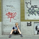 Ein Junge sitzt auf der Straße vor einer beschmierten Hauswand.