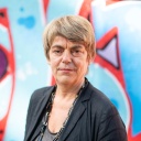 Amelie Deuflhard, die Intendantin der Kulturfabrik Kampnagel, steht vor einer mit Graffiti besprüh
        ten Wand und blickt in die Kamera