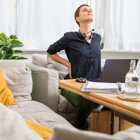 HomeOffice: Frau arbeitet vom Sofa aus am Computer und hat Rückenschmerzen
