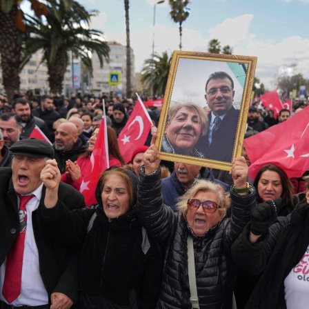 Ein Demonstrantin reckt ein gerahmtes Foto von ihr und Imamoglu in die Höhe. Um sie herum tausende weiterer Demonstranten u.a. mit türkischen Flaggen.