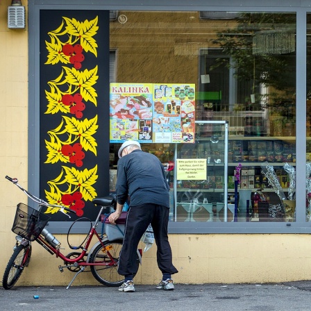 Ein älterer Mann steht mit seinem Fahrrad vor einem russischen Spezialitätengeschäft.