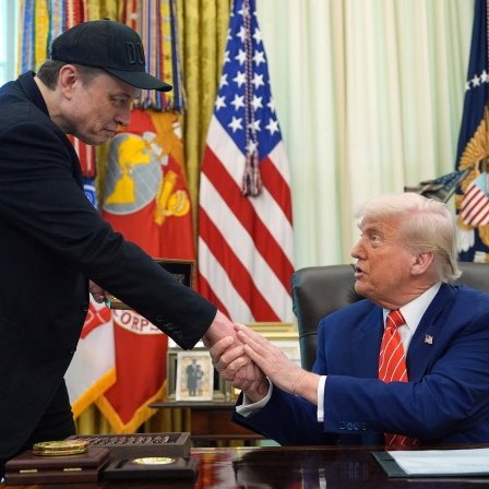 Donald Trump hält eine Hand von Elon Musk in seinen.