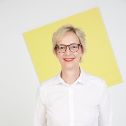 Christine Regitz hat kurzes, blondes Haar. Sie trägt eine weiße Bluse und eine braune Hornbrille.