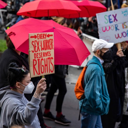 Auf einer Demonstration hält eine Frau ein Schild mit der Aufschrift "Every sex worker deserves rights". Im Hintergrund sind rote Regenschirme zu sehen.