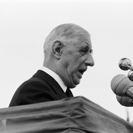 Der französische Staatspräsident Charles de Gaulle steht vor Mikrofonen an einem Pult und hält eine Rede.