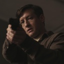 Ein Mann steht mit einer gezückten Pistole in einem dunklen Raum