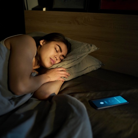 Frau schläft mit Handy beim Bett