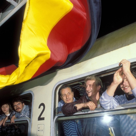 DDR-Flüchtlinge im Zug während der Ankunft in Hof im Oktober 1989. Vor dem Zug weht eine bundesdeutsche Flagge.
