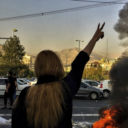  Eine Frau steht während einer Demonstration nach dem Tod der 22-jährigen Mahsa Amini vor einem brennenden Autoreifen und zeigt das Victory-Zeichen. Archivbild: 30.09.2022 