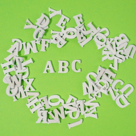 Weiße Holzbuchstaben wild auf grünem Untergrund verteilt - einzig die Buchstaben ABC kann man lesen.