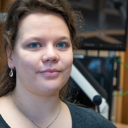 Portrait von Julia Nagel (junge Frau mit langen braunen Haaren sitzt im MDR-Studio neben einem Mikrofon)