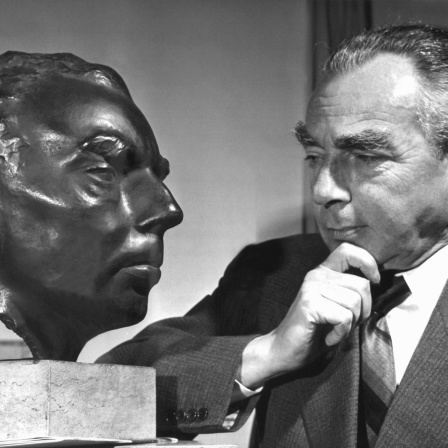 Erich Kästner betrachtet nachdenklich sein Ebenbild als Bronzebüste. Foto von 1959
