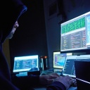 Symbolbild Cyberkriminalität - Kaputzenmann vor Computermonitoren