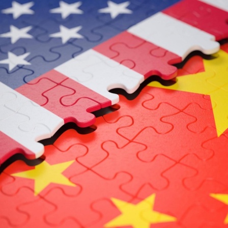 Symbolbild: Ein unfertiges Puzzle, das einen Teil der Flagge der USA zeigt, liegt über einem anderen Puzzle, das einen Teil der Flagge Chinas zeigt. 