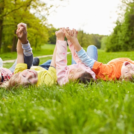 Kinder liegen auf einer Wiese und halten sich an den Händen