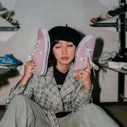 Frau hält sich rosa Sneaker an die Wangen; sie umgeben von Regalen voller Schuhe