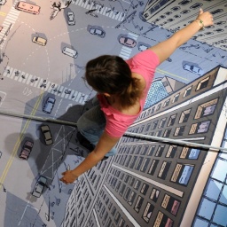 Eine Frau balanciert auf einem Seil über eine am Boden aufgemalte Stadt.